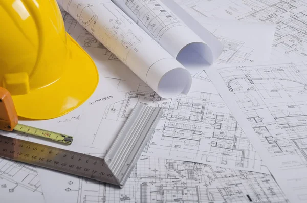 Yellow construction helmet and heap of project drawings. Royalty Free Stock Images