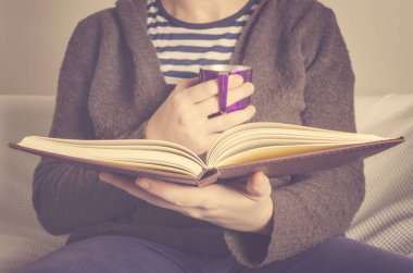 Bir kanepe ile ilgili bir kitap okuma ve bir fincan kahve tutan genç adam