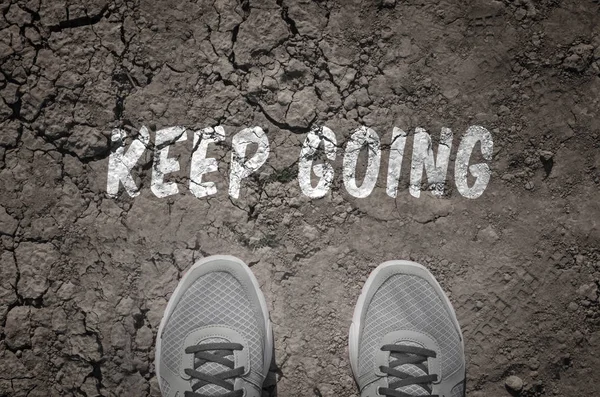 Sneakers on dry land with the text: Keep going — Stock Photo, Image