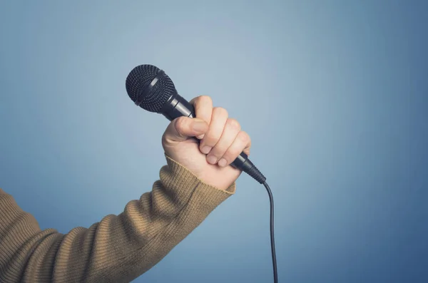Male hand holding microphone on blue background