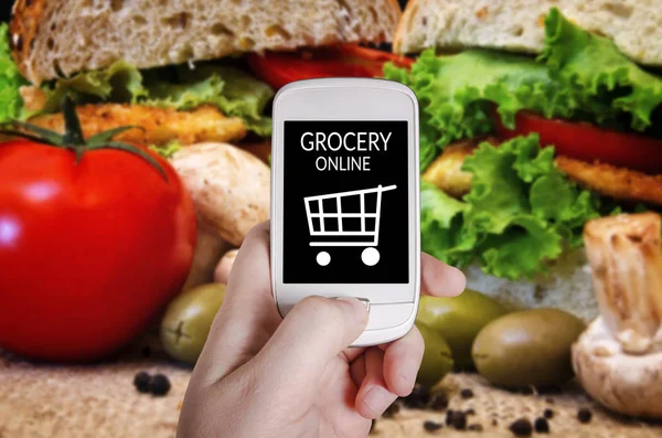Kezében okos telefon a homályos élelmiszer-háttér — Stock Fotó