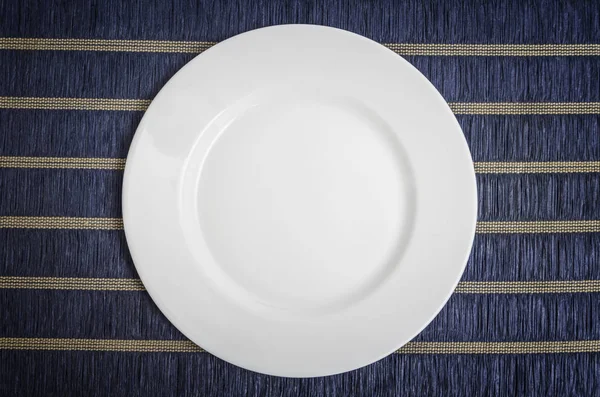 Piring putih kosong pada latar belakang taplak meja biru — Stok Foto