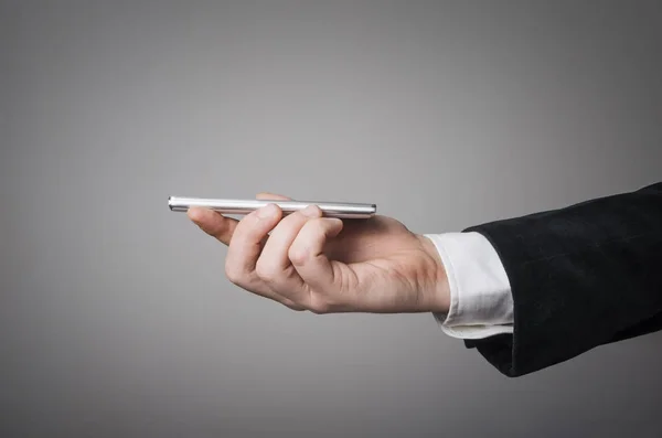 Elegante mano de hombre de negocios sosteniendo un teléfono inteligente frente a un concepto de fondo de pared gris claro vacío — Foto de Stock