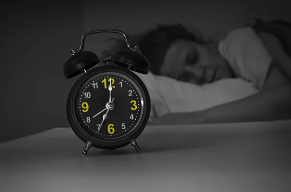 Focus on the alarm clock in front of sleeping woman at night in the bedroom — Stock Photo, Image