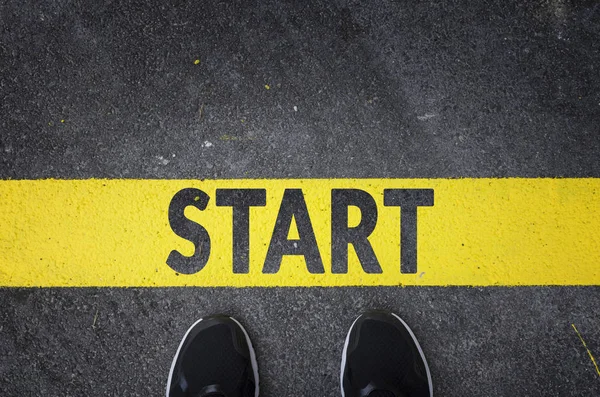 Sneakers on asphalt road with yellow start line top view — Stock Photo, Image