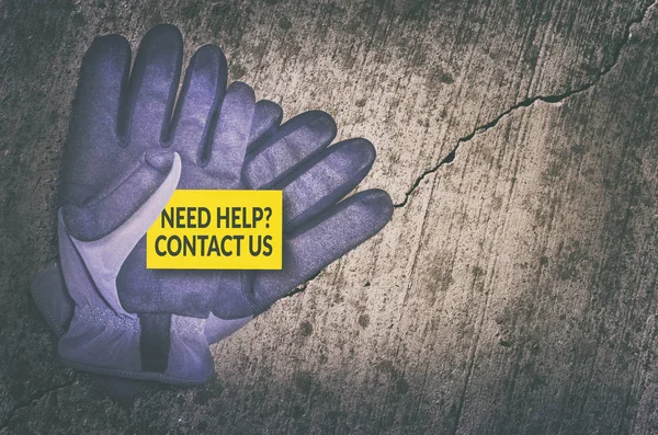 Precisa de ajuda? Entre em contato conosco cartão em luvas de proteção sobre fundo de concreto rachado . — Fotografia de Stock