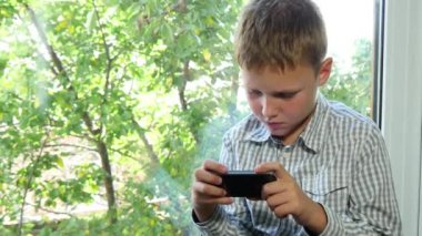 Onun Smartphone kullanarak bir cam kenarında oturan çocuk