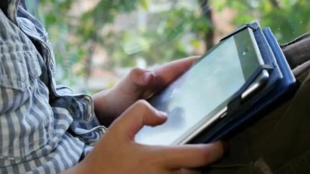 Niño sentado junto a una ventana usando su tableta — Vídeo de stock