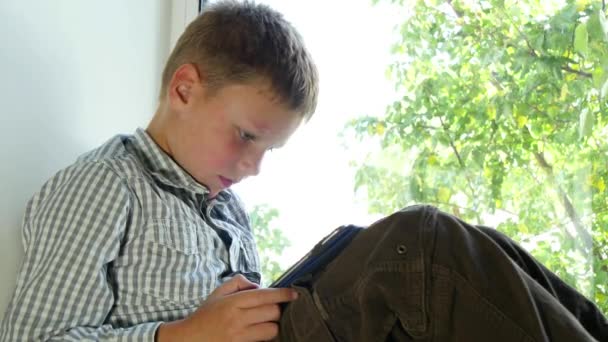 Jongen zitten door een venster met behulp van zijn Tablet — Stockvideo