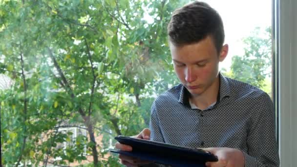 Nastolatek siedzi przez okno przy użyciu jego Tablet — Wideo stockowe