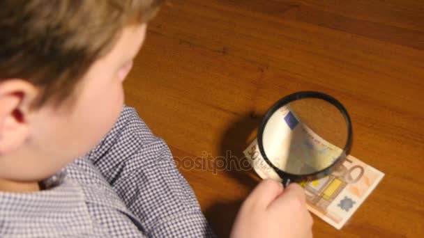 虫眼鏡でユーロ紙幣を調べる少年 — ストック動画