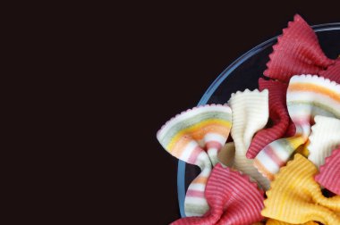 Siyah bir arka plan üzerinde izole orijinal İtalyan makarna. Makarna siyah bir arka plan üzerine düşündüm. Çok renkli makarna. Bir kelebek şeklinde güzel makarna.                      