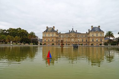 Paris'teki Lüksemburg Sarayı önünde bir su birikintisi üzerinde bir oyuncak tekne yelken. Lüksemburg Sarayı güzel bir bahçesi yeşilliklerle çevrilidir. Lüksemburg Bahçeleri. Çeşme ve gölet Lüksemburg Sarayı önünde yeşil su ile.