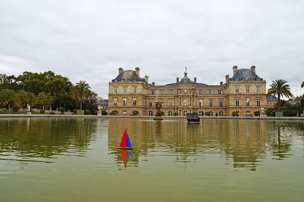 Paris'teki Lüksemburg Sarayı önünde bir su birikintisi üzerinde bir oyuncak tekne yelken. Lüksemburg Sarayı güzel bir bahçesi yeşilliklerle çevrilidir. Lüksemburg Bahçeleri. Çeşme ve gölet Lüksemburg Sarayı önünde yeşil su ile.