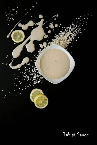 Ev yapımı tahini sosu, susam tohumları ve siyah arka planda limon. Vejetaryen yemeği. Sağlıklı yiyecekler. Tanıtım broşürü ve poster. Düz yatıyordu.