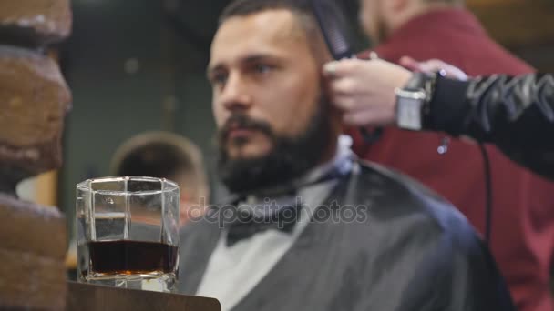 Vaso de whisky en un fondo de hombre consiguiendo corte de pelo por peluquero mientras está sentado en la silla en la barbería. Barbería tema . — Vídeos de Stock