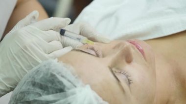 Güzel genç kadın botox enjeksiyon Kliniği'nde oluyor. O oturan ve gülümseyerek. Doktor şırınga kaşlarını yakınındaki dikkatle tutuyor