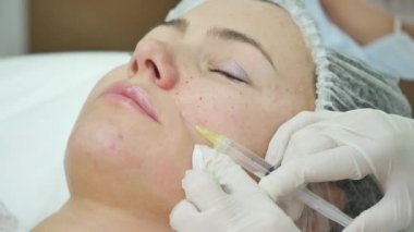 Güzel genç kadın botox enjeksiyon Kliniği'nde oluyor. O oturan ve gülümseyerek. Doktor şırınga kaşlarını yakınındaki dikkatle tutuyor
