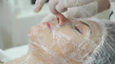 Güzellik uzmanı kadın yüzü krem maske uygulayarak el kapatın. Fırça tutuyor. Güzel genç kadın gevşeme ile yatıyor