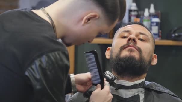 Close-up handsome young bearded man getting beard grooming in modern barbershop. — Stock Video