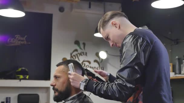 Serio joven barbudo cortarse el pelo por peluquero. Barbería Theme. Movimiento lento . — Vídeo de stock