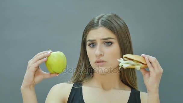 Hard choice: apple or burger, flustered girl decided to go on a diet — Stock Video