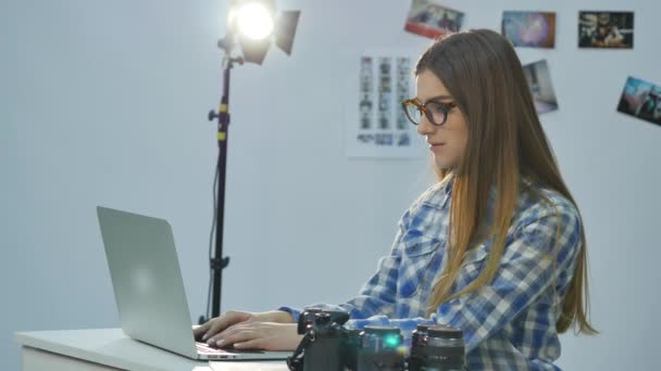 Samica fotograf pracuje w jej zdjęcie profesjonalne studio z laptopa, aparat fotograficzny i sprzętu oświetleniowego — Wideo stockowe