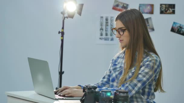 Samica fotograf pracuje w jej zdjęcie profesjonalne studio z laptopa, aparat fotograficzny i sprzętu oświetleniowego — Wideo stockowe