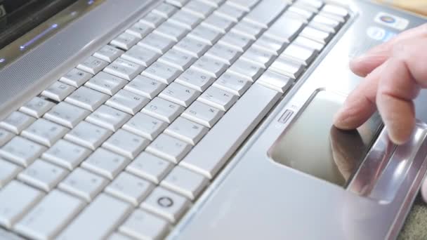 Людина використовує тачпад на клавіатурі ноутбука з пальцем з синім світлим відтінком — стокове відео