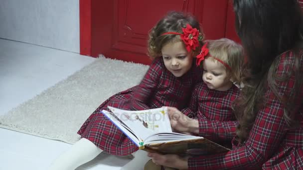 Feliz Navidad y Felices Fiestas Bonita mamá joven leyendo un libro a sus hijas lindas. Sesión de fotos con luz de flash — Vídeos de Stock