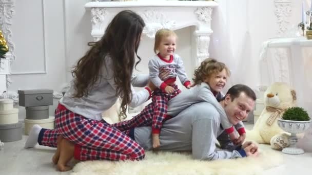 Mladá rodina sedí na podlaze na vánočním ránu v pyžamu, s úsměvem. Focení s bleskem