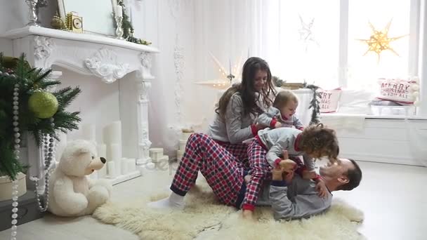 Feliz familia joven sentada en el suelo en la mañana de Navidad en pijama, sonriendo. Sesión de fotos con luz de flash — Vídeos de Stock