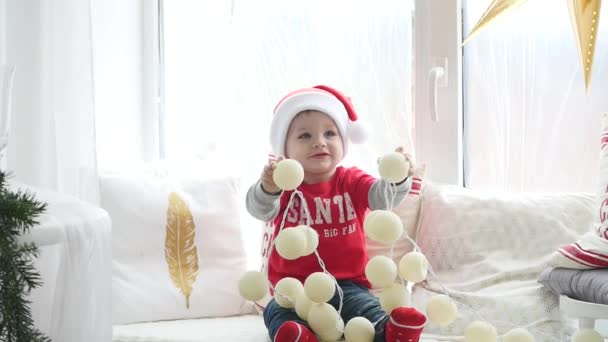 Entzückender kleiner Junge, der zu Hause mit Weihnachtsdekoration und leuchtenden Girlanden spielt. Fotoshooting mit Blitzlicht — Stockvideo