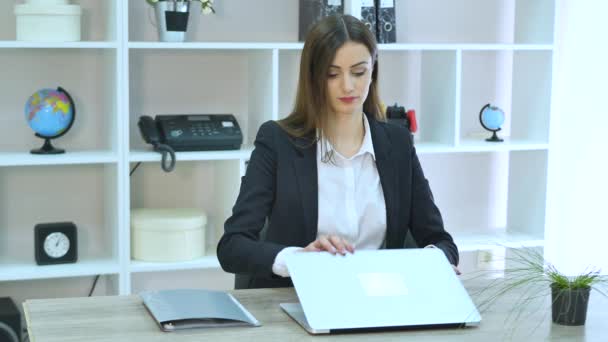 Zijaanzicht van zakenvrouw praten aan de telefoon en zitten door de tabel met laptop in office — Stockvideo