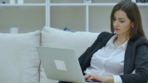 Joven mujer de negocios sentada en el sofá, trabajando con computadora portátil — Vídeos de Stock