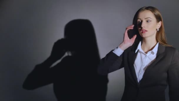 Joven mujer elegante hablando en el teléfono móvil sobre fondo negro con sombra — Vídeo de stock