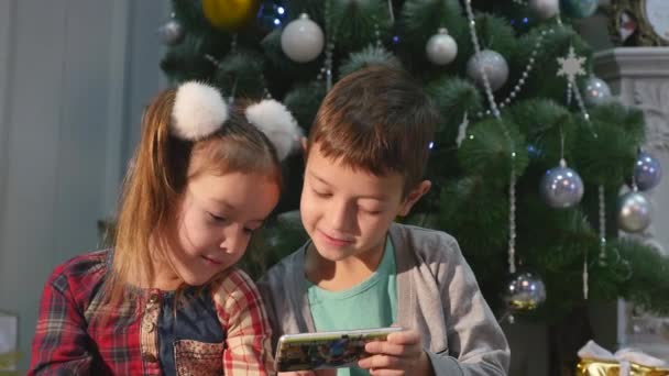 Niño jugando en el teléfono móvil, los niños y el teléfono inteligente cerca del árbol de Navidad — Vídeo de stock