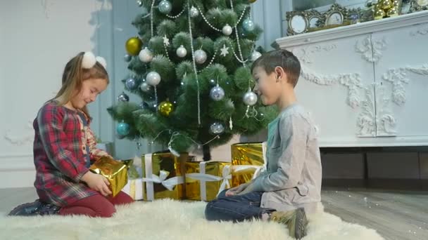 Kleine broer en zus uitpakken cadeaus Het concept van Kerstmis en Nieuwjaar — Stockvideo