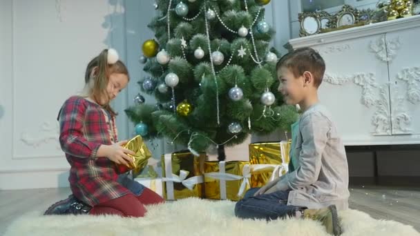 Hermanito y hermanita desempaquetan regalos. El concepto de Navidad y Año Nuevo — Vídeos de Stock