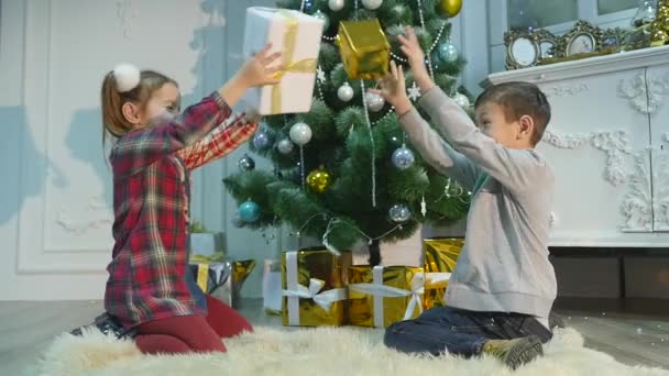 Kleine broer en zus uitpakken cadeaus Het concept van Kerstmis en Nieuwjaar — Stockvideo