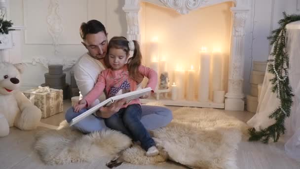 Jonge vader zit met dochter bij open haard en het vertellen verhaal op kerstavond — Stockvideo