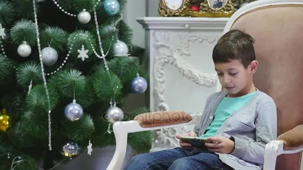Niño jugando en el teléfono móvil, los niños y el teléfono inteligente cerca del árbol de Navidad — Vídeo de stock