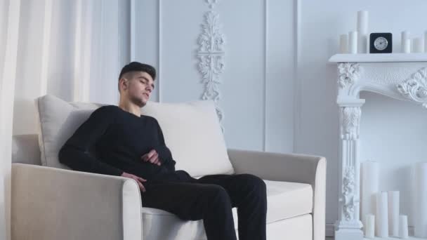 Tinggal berhubungan di rumah. Pemuda ceria memegang ponsel dan tersenyum sambil berbaring di sofa — Stok Video