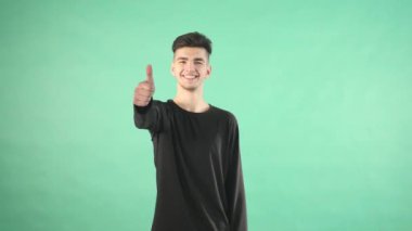 yeşil bir arka plan üzerinde genç adam başparmak yukarıya ile gülümseyen izole