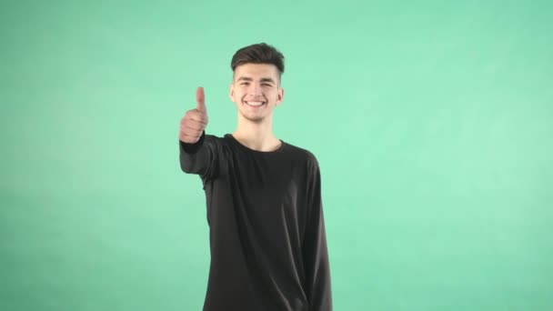 Junger Mann lächelt mit erhobenem Daumen auf grünem Hintergrund — Stockvideo