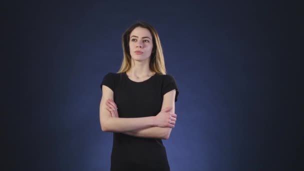 Серьезная молодая женщина думает о чем-то на темном фоне — стоковое видео