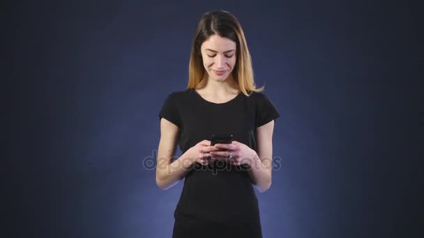 Sonriendo hermosa mujer mensajes de texto con su teléfono negro fondo — Vídeos de Stock