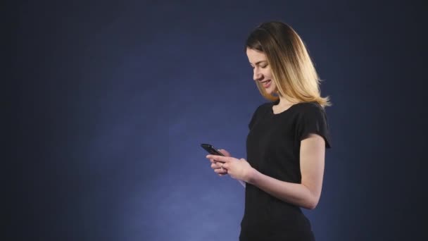 Mooie vrouw texting met haar telefoon zwarte achtergrond zijaanzicht glimlachen — Stockvideo