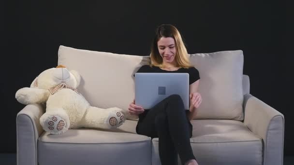 Chica con un portátil en el sofá. fondo negro — Vídeos de Stock