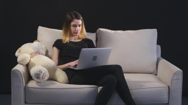 Дівчина з ноутбуком на дивані. чорний фон — стокове відео